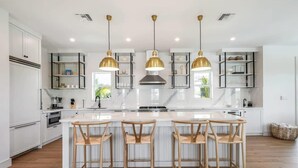 Una cocina moderna con armarios blancos, una isla central con taburetes y lámparas colgantes.
