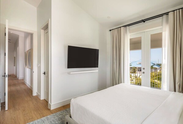 A hotel room with a bed, a TV mounted on the wall, and a balcony with curtains.