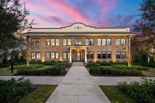 A large, two-story building with a symmetrical facade, a central entrance with a small porch, and a brick exterior.