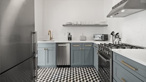 Una cocina moderna con armarios grises, suelo a cuadros blanco y negro, un refrigerador de acero inoxidable, lavavajillas, estufa a gas y una lámpara colgante.