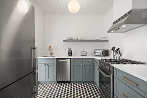 Une cuisine moderne avec des meubles gris, un carrelage noir et blanc, un réfrigérateur en acier inoxydable, un lave-vaisselle, une cuisinière à gaz et un luminaire suspendu.