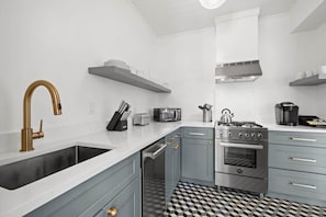 Uma cozinha moderna com fogão de aço inoxidável, forno embutido, micro-ondas e pia com torneira dourada.