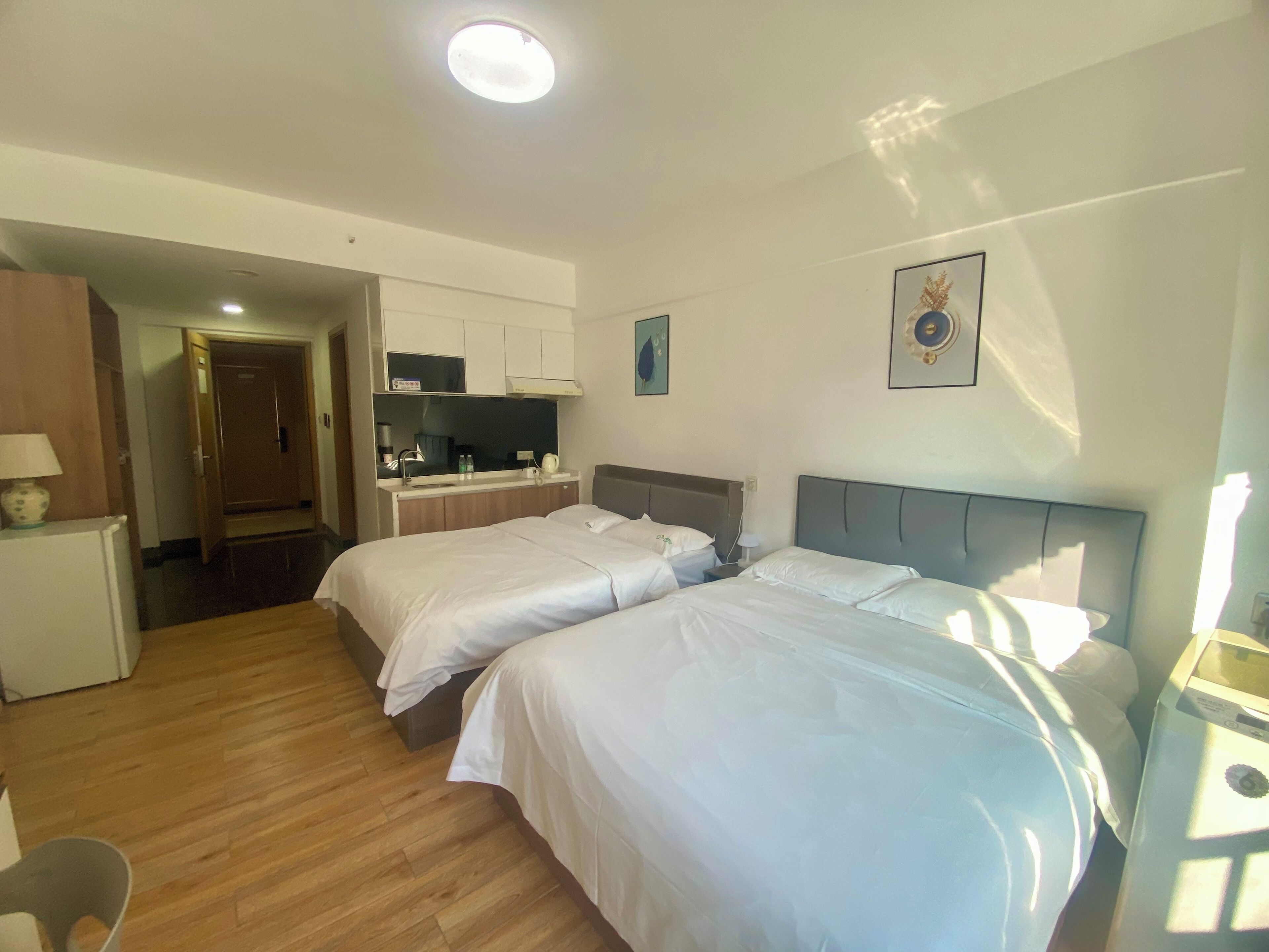 A hotel room with two beds, a desk, a small kitchenette, and a bathroom.