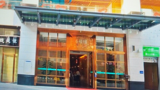 A building with a large glass entrance, wooden beams on the ceiling, and a green sign on the right. - ManGo Holiday Internation Apartment (Dongguan)