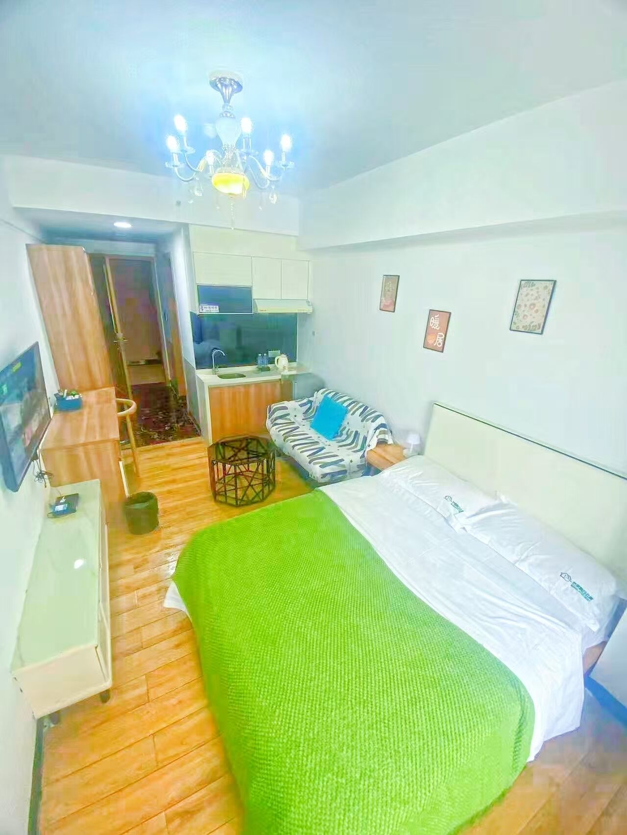 A hotel room with a bed, a desk, a chair, a small kitchenette, and a bathroom.