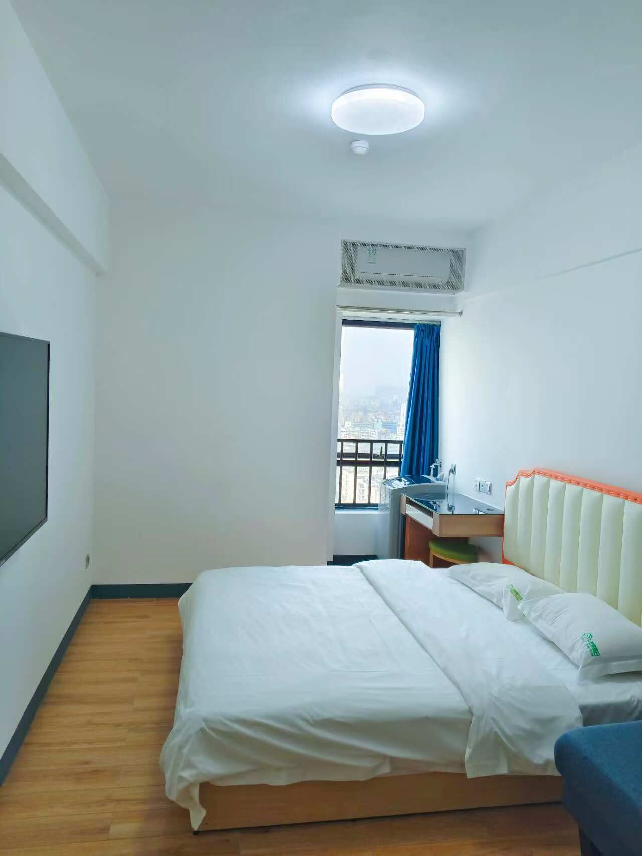 Ein Hotelzimmer mit einem Bett, einem Schreibtisch mit Stuhl, einem Fenster mit Vorhängen und einer Klimaanlage.