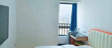 Ein Hotelzimmer mit einem Bett, einem Schreibtisch mit Stuhl, einem Fenster mit Vorhängen und einer Klimaanlage.