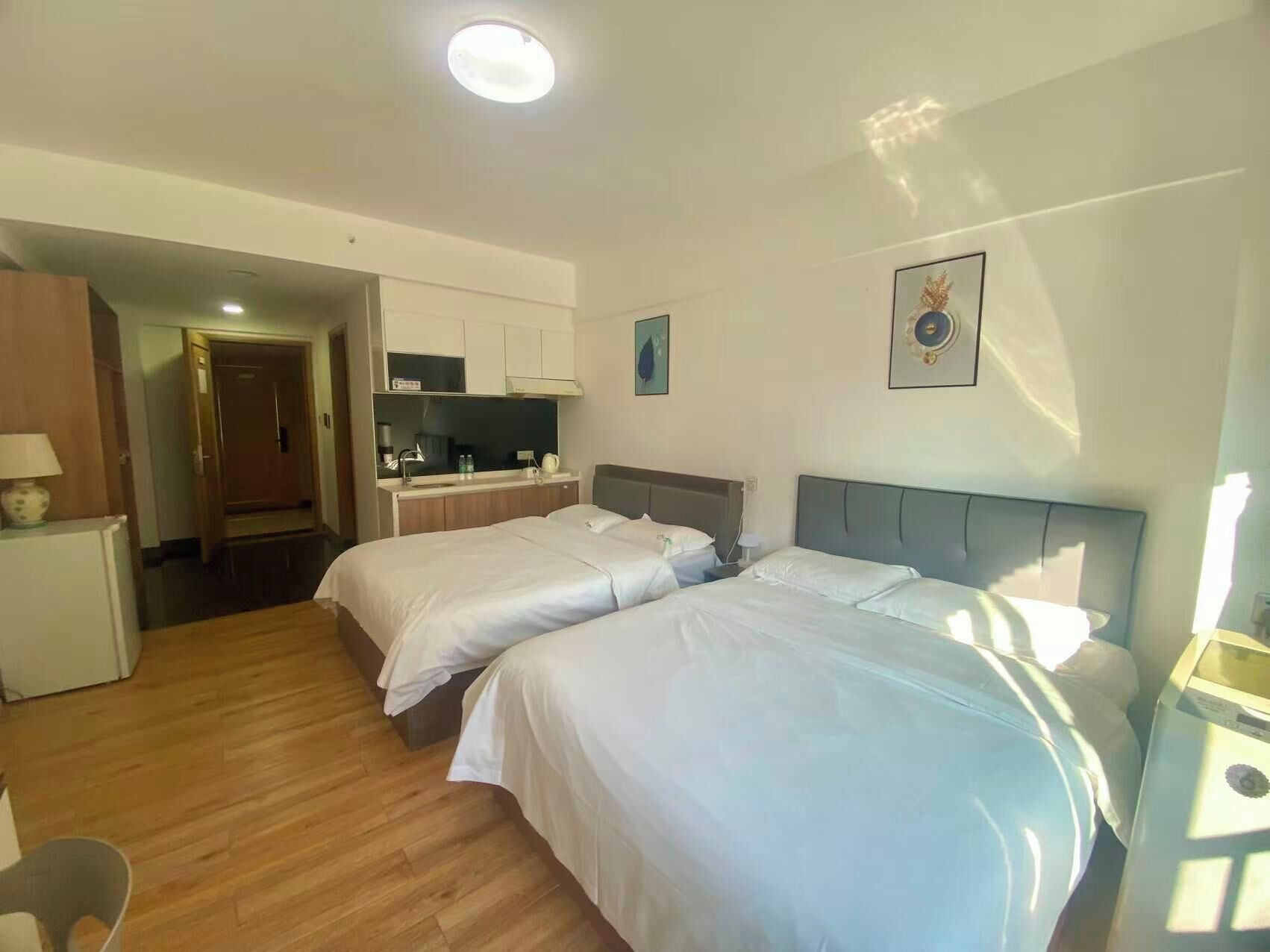A hotel room with two beds, a kitchenette, a desk, and a chair.