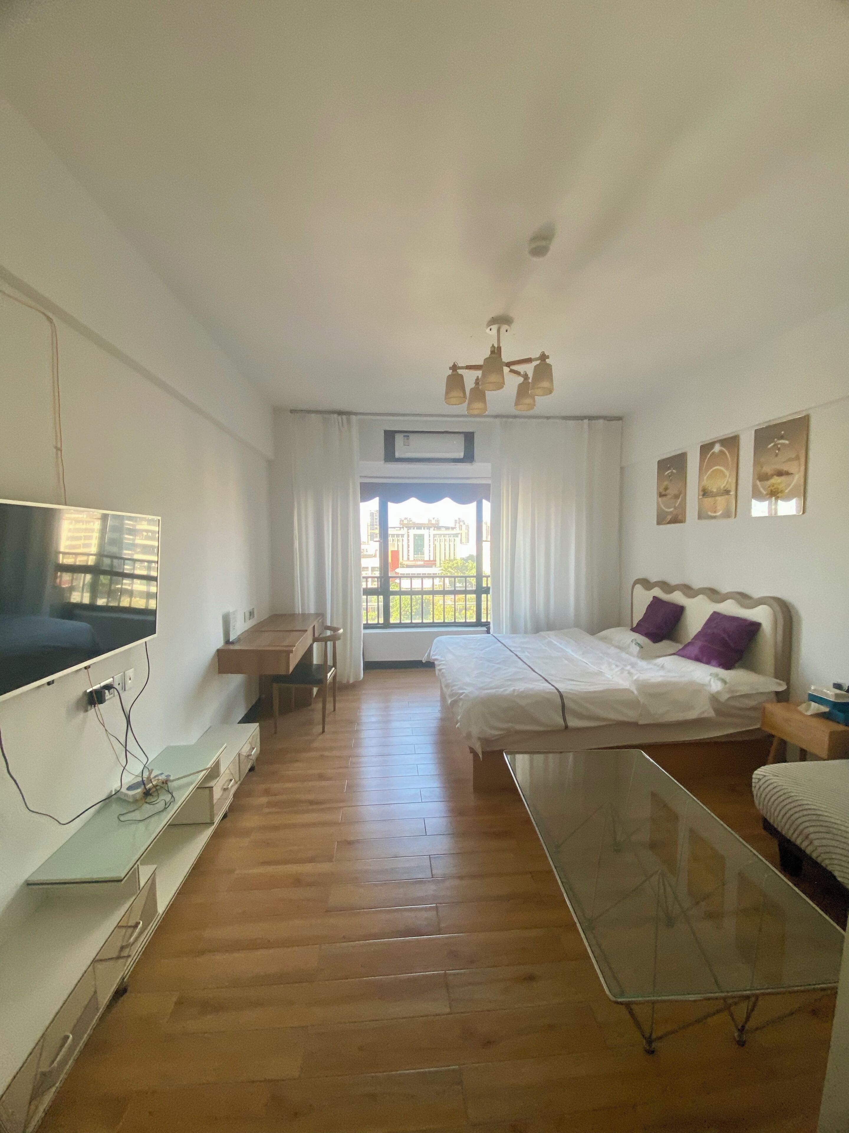 A modern bedroom with a bed, a desk, a TV, and a balcony view.