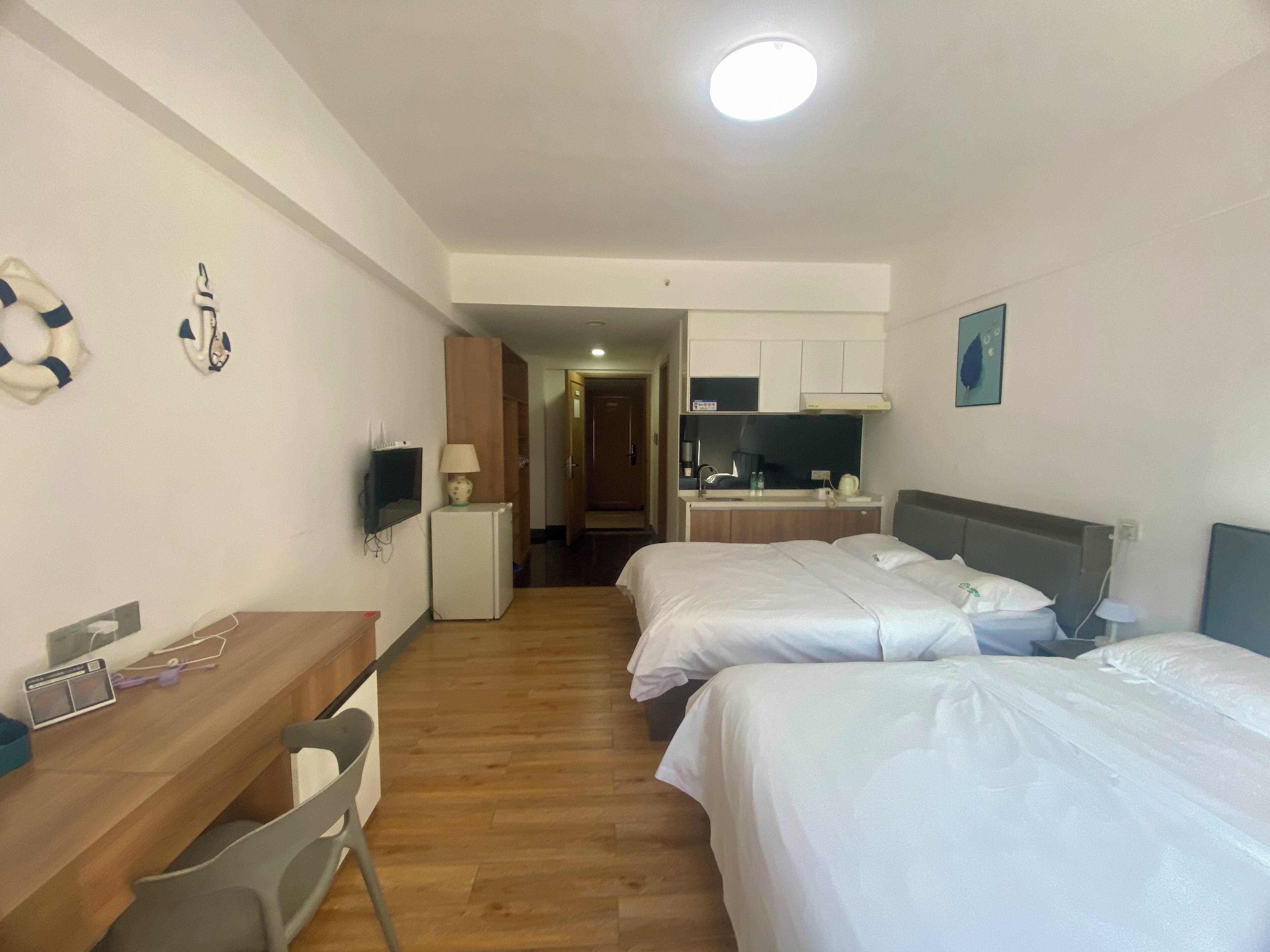 Quarto de hotel com duas camas, uma mesa, uma kitchenette pequena e uma televisão.