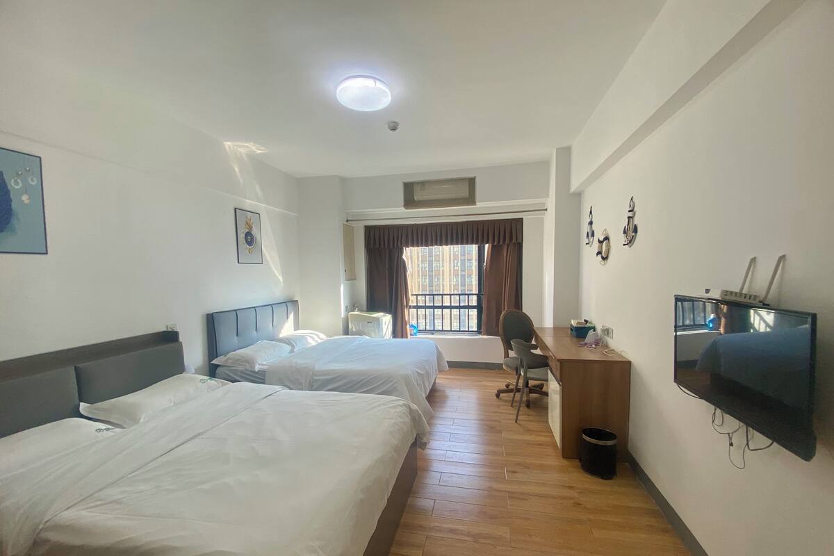 Una habitación de hotel con dos camas, un escritorio, una silla, un televisor y una ventana con cortinas.