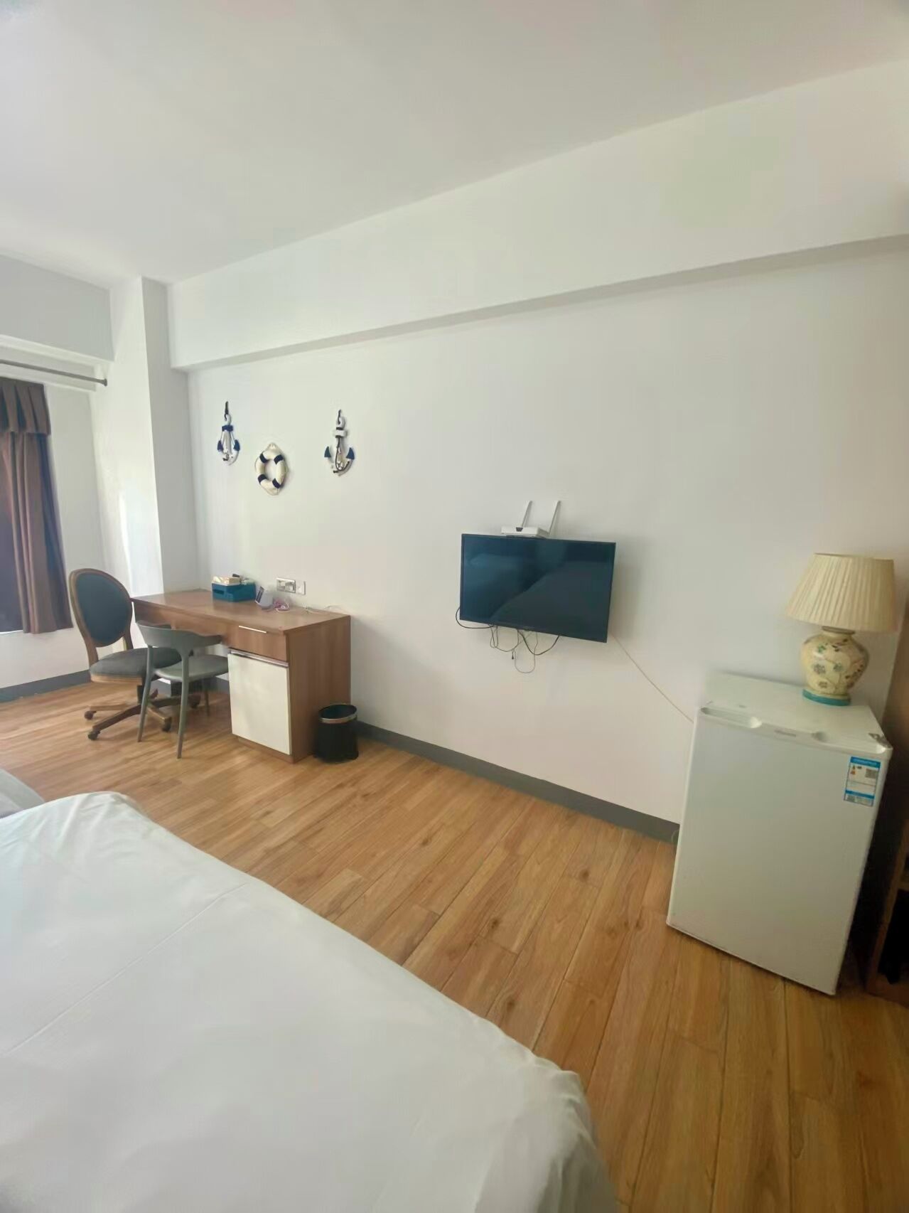 Een hotelkamer met een bed, bureau, stoel, televisie, lamp en een kleine koelkast.