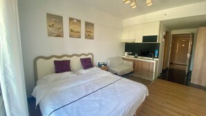 A hotel room with a bed, a small kitchenette, and a bathroom visible through an open door. - ManGo Holiday Internation Apartment (Dongguan)
