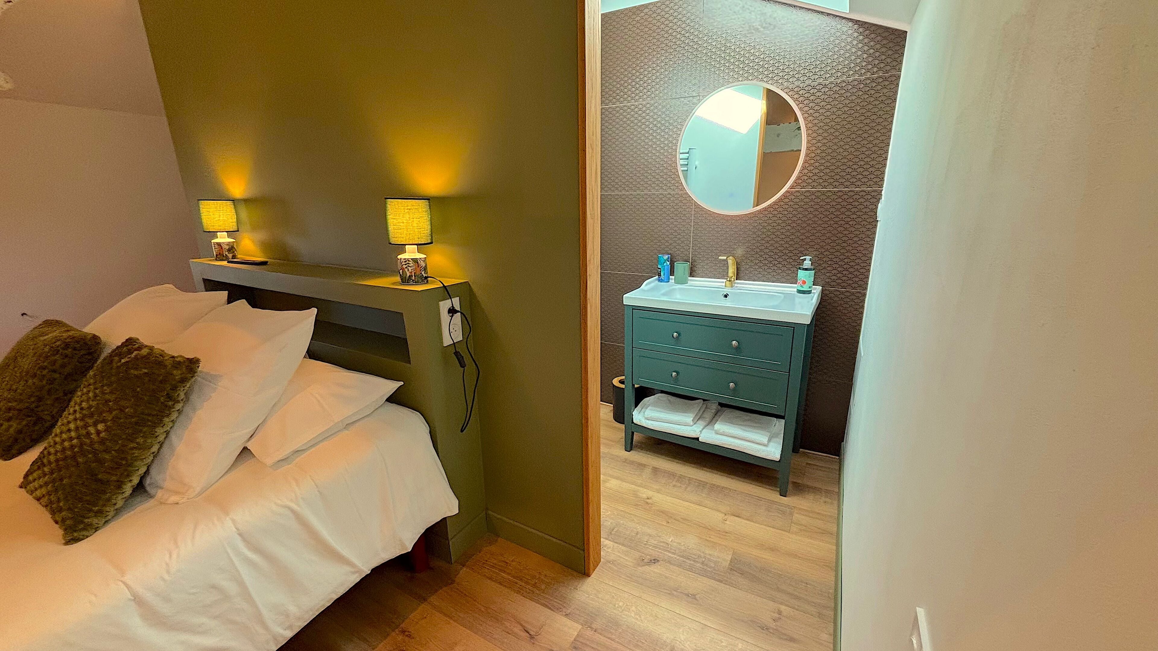 Une chambre d’hôtel avec un lit, des lampes de chevet, une coiffeuse avec un miroir et une petite poubelle.
