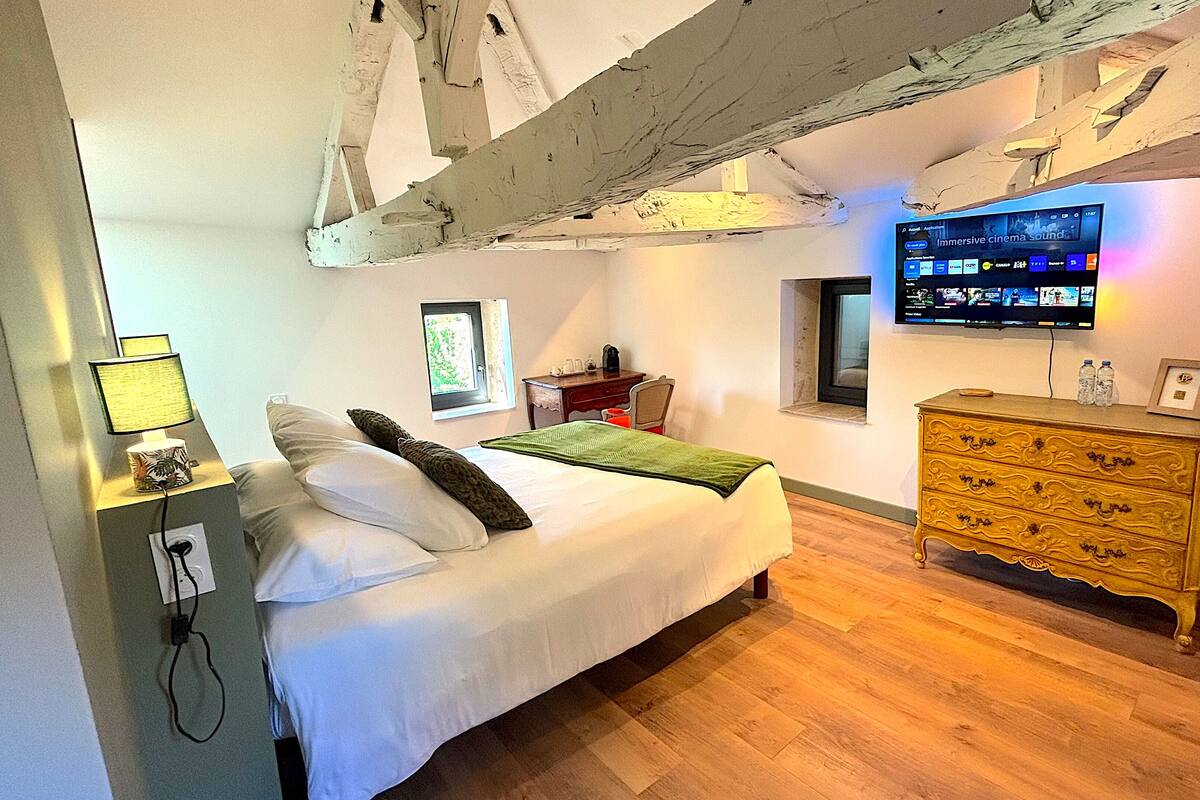Un dormitorio con cama, cómoda, televisor montado en la pared y ventana.