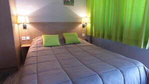 Una habitación de hotel con una cama grande, dos almohadas verdes, un cabecero de madera, dos lámparas de noche y una cortina verde.