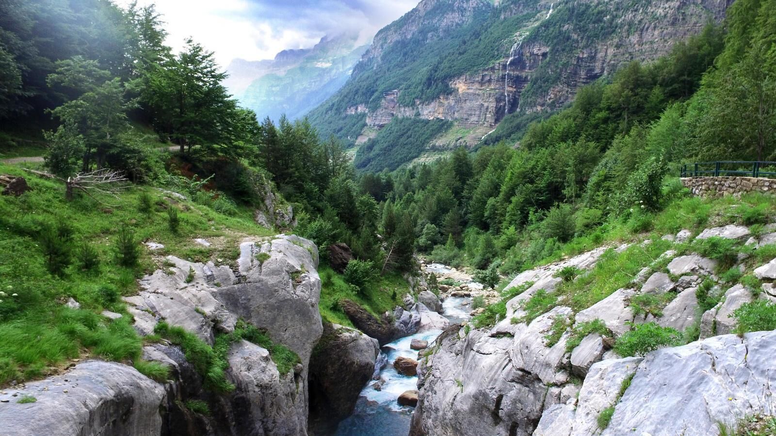 A mountainous landscape with a river flowing through a rocky gorge, surrounded by dense green forest.