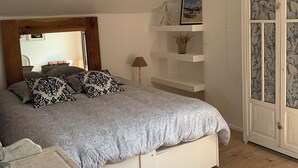 Un dormitorio con cama, mesita de noche, lámpara, armario y una pequeña mesa con una cesta.