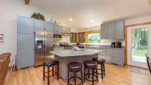 A modern kitchen with grey cabinets, a stainless steel refrigerator, a microwave, and a large island with stools. - Secluded Lake Escape w/ Dock, Fire Pit & Views (Oakland)