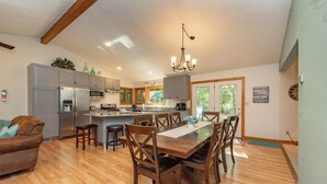 A spacious kitchen with modern appliances, a dining area with wooden chairs, and a chandelier. - Secluded Lake Escape w/ Dock, Fire Pit & Views (Oakland)