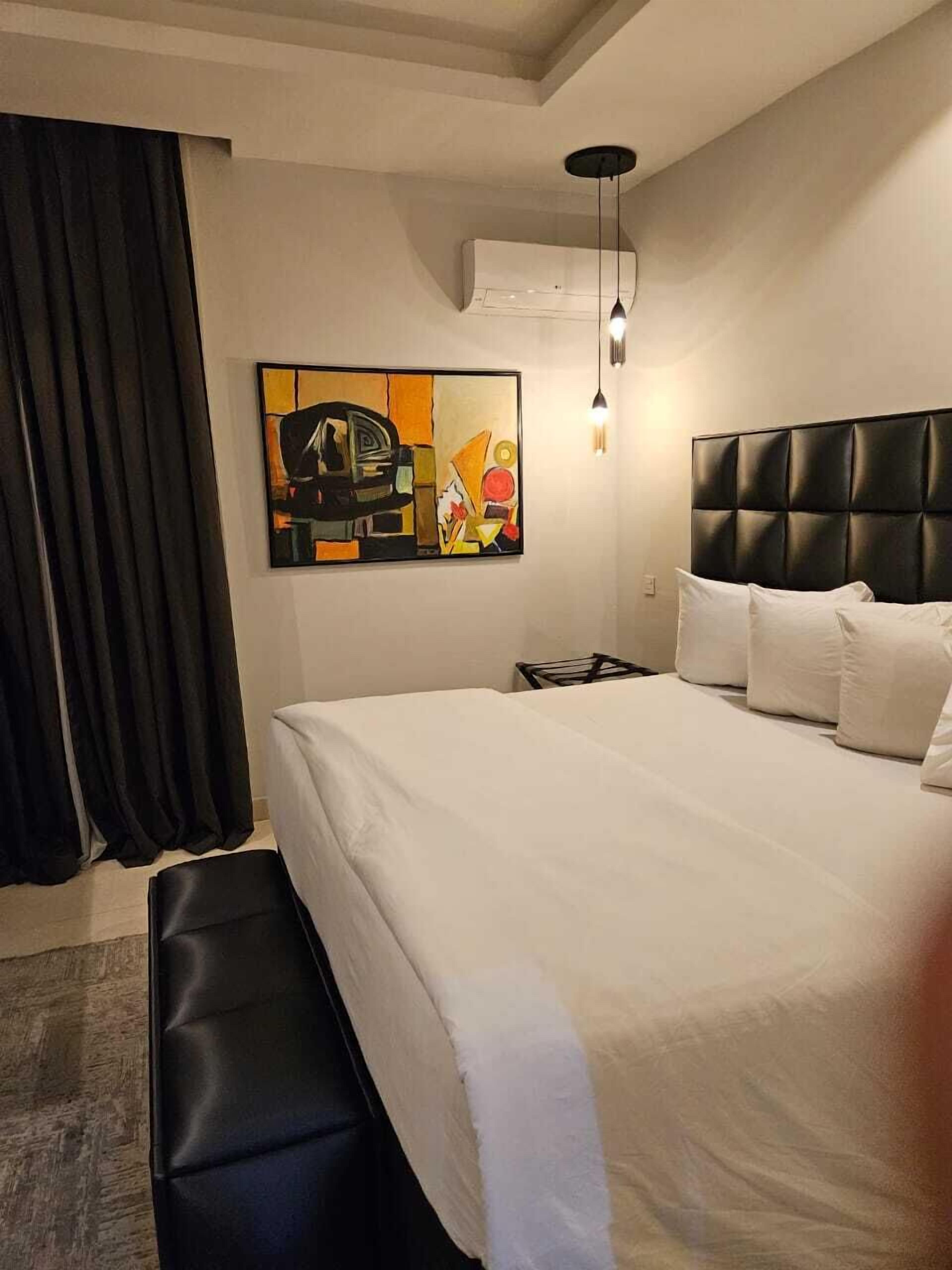 Ein modernes Hotelzimmer mit einem großen Bett, einem schwarzen Kopfteil, einem Bild an der Wand und einem Fenster mit Vorhängen.