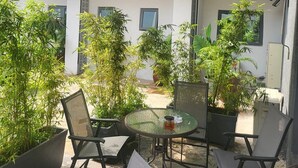 An outdoor patio area with a round table and chairs, surrounded by potted plants and a covered seating area. - Melbrooke Park Hotel (Lekki)