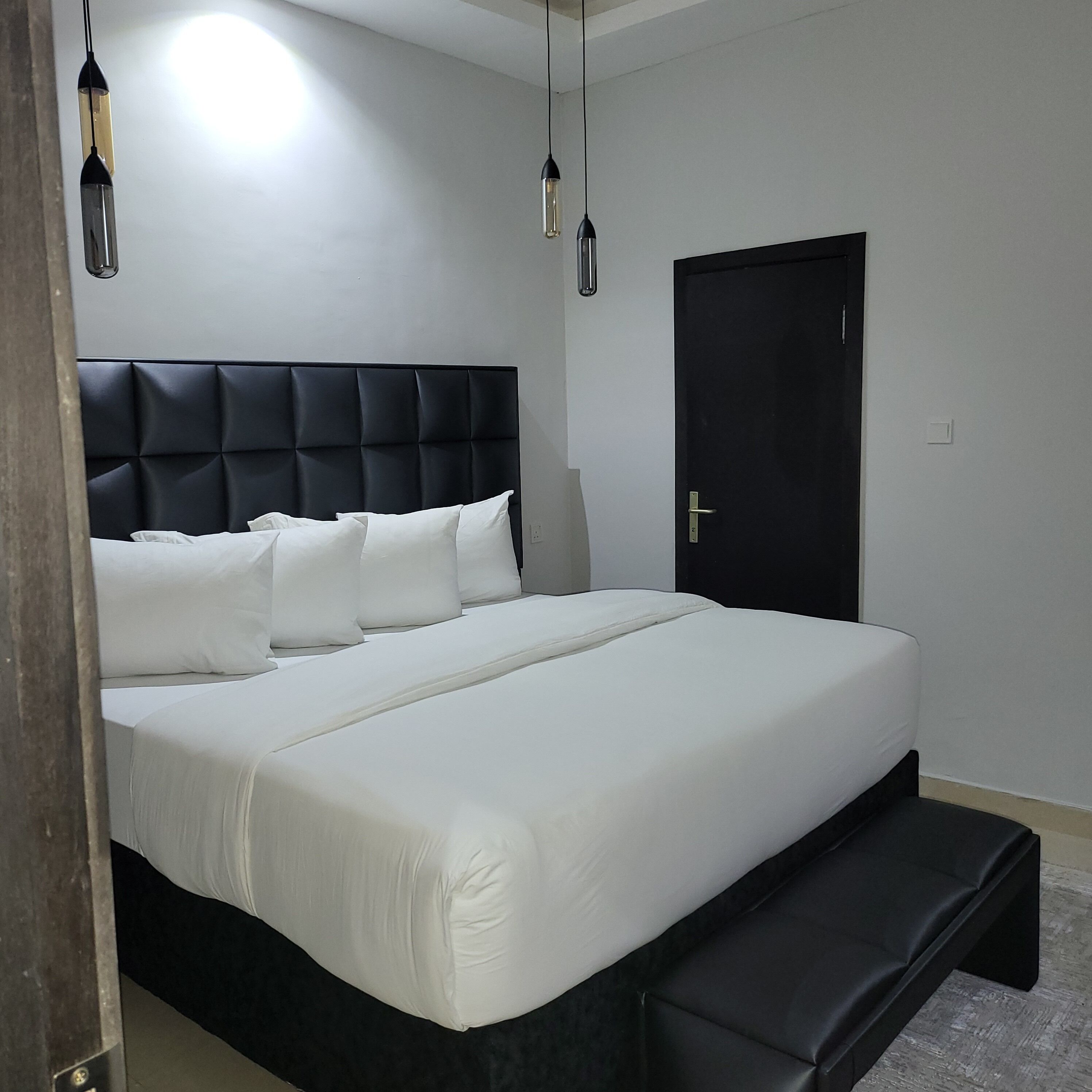 Un dormitorio moderno con una cama grande, un banco al pie y una puerta.