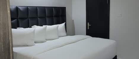 A modern bedroom with a large bed, a bench at the foot, and a door.