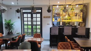 A modern restaurant interior with wooden tables and chairs, a bar area with illuminated shelves, and a large window with greenery visible outside. - Melbrooke Park Hotel (Lekki)