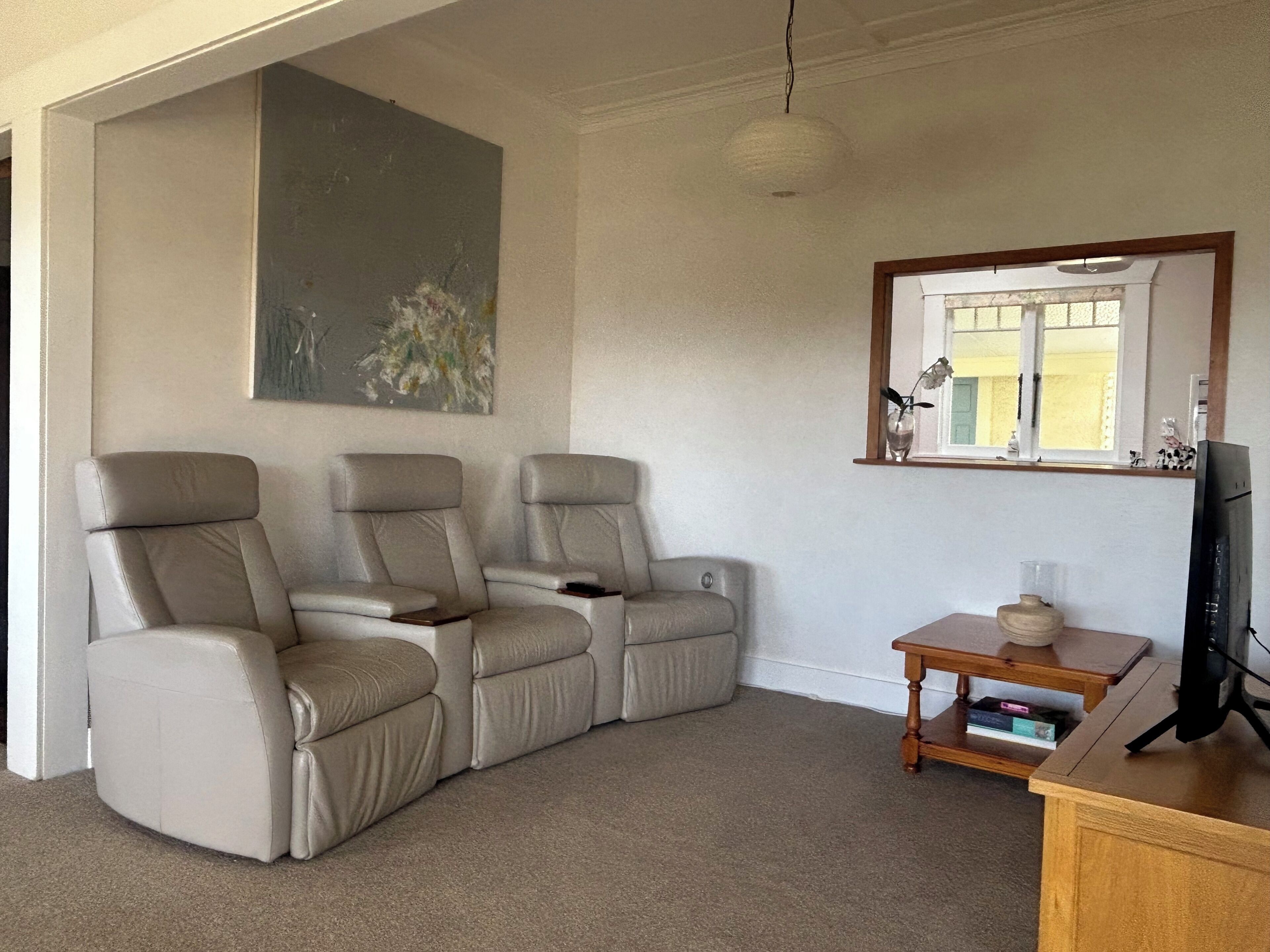 A room with a beige sectional sofa, a small wooden table with a television, and a window with a view of a building.