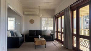 Una sala de estar con sofá, mesa de centro y un ventanal con cortinas.