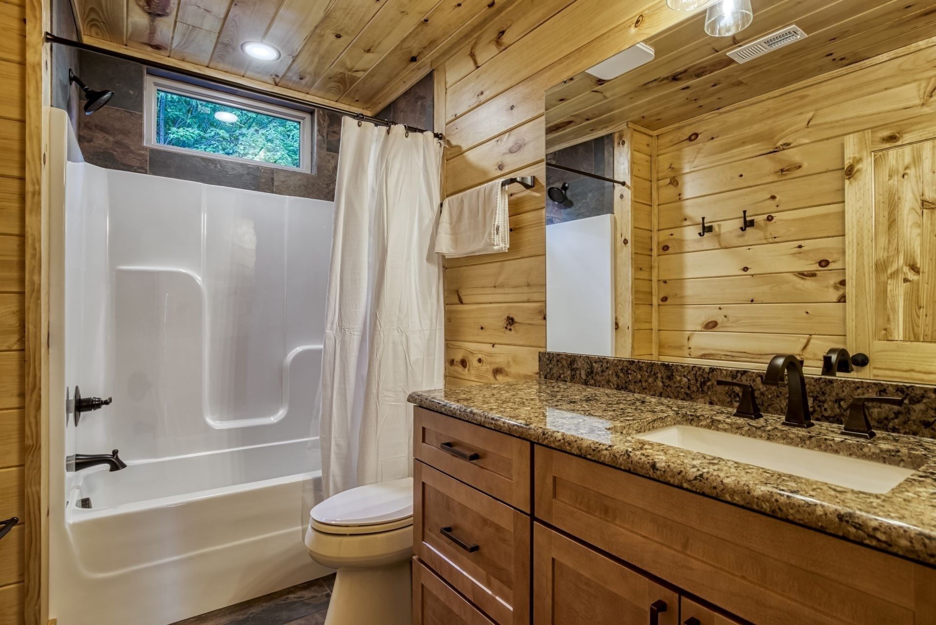Une salle de bain rustique, avec des murs en bois, comprenant une baignoire, des toilettes, un meuble-lavabo et un miroir.