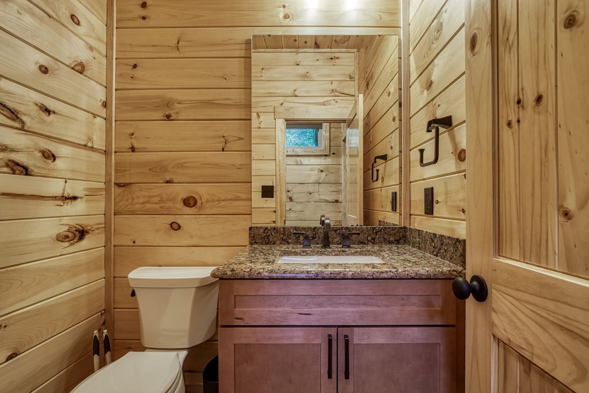Een kleine badkamer met houten wanden, een granieten aanrecht, een wastafel, een toilet en een spiegel.