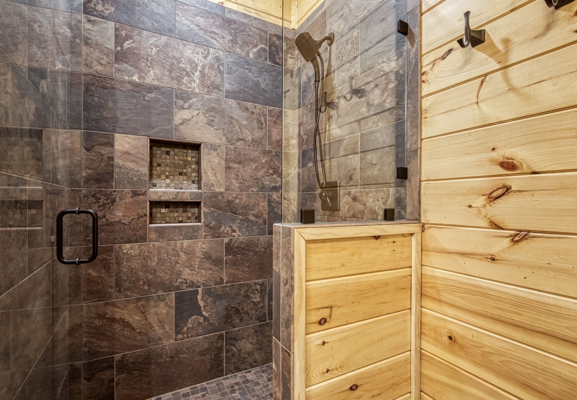 Ein Badezimmer mit dunklen Marmorfliesen, einem Holzkosmetikschrank und einer Duschkabine.