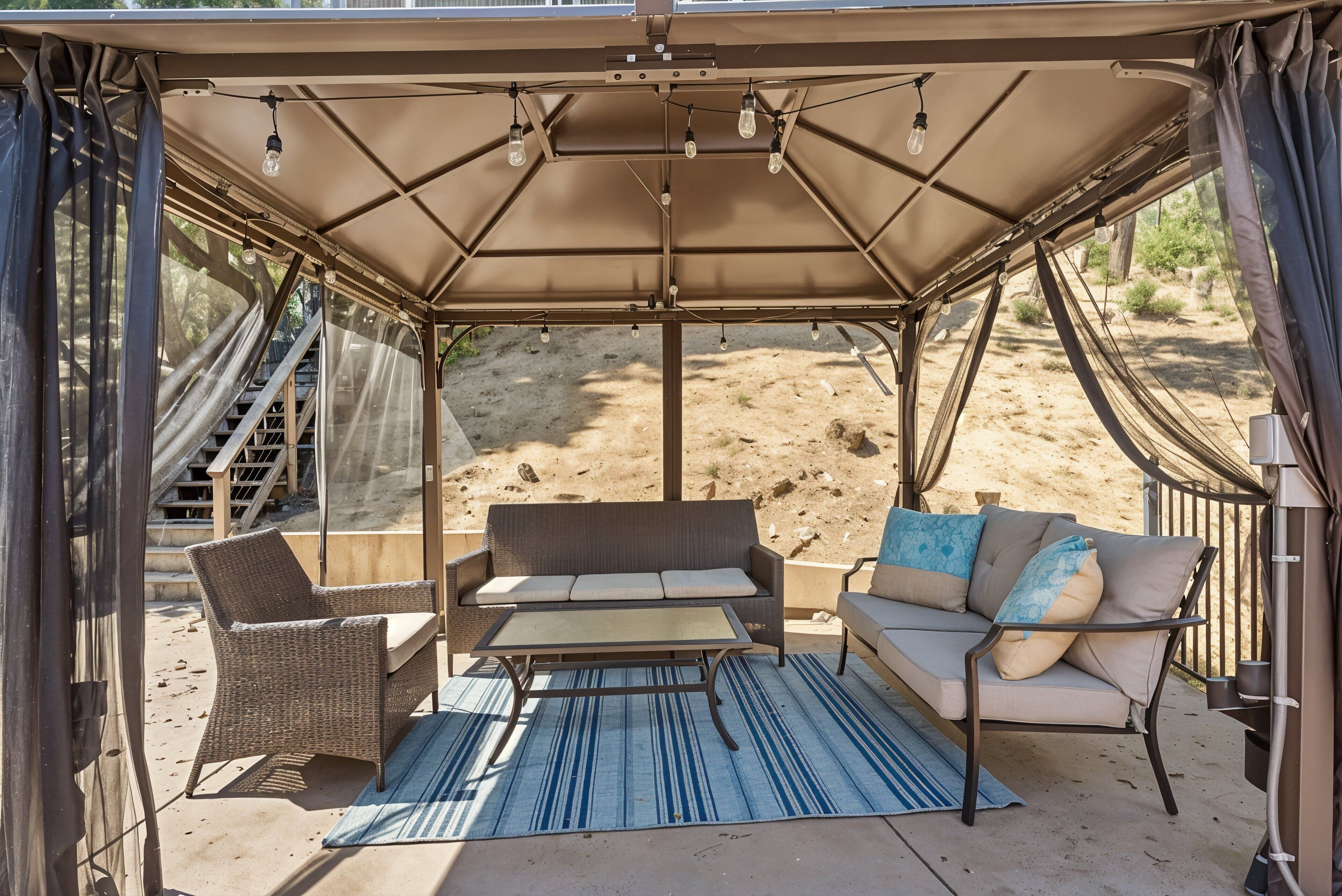 A covered outdoor seating area with wicker furniture and a table, featuring a view of a desert landscape.