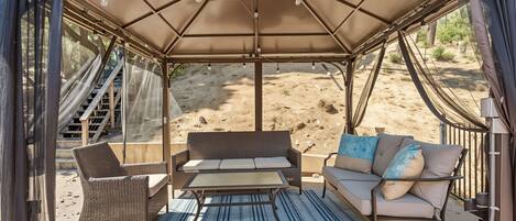 A covered outdoor seating area with wicker furniture and a table, featuring a view of a desert landscape.