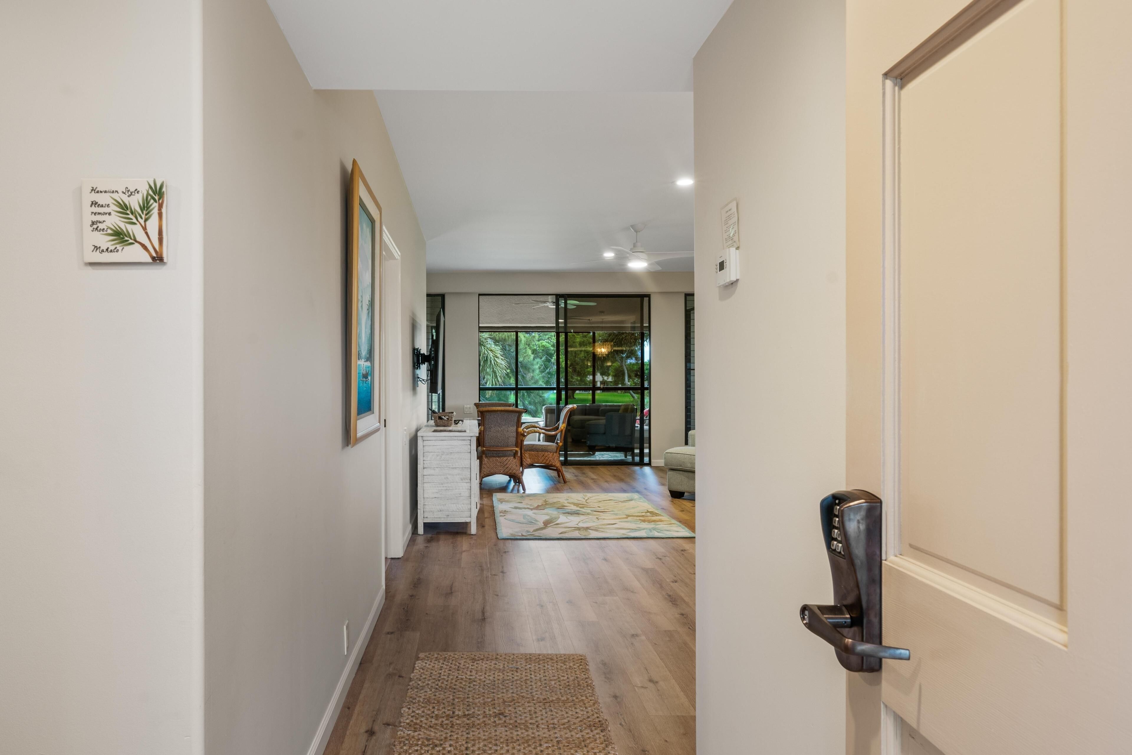 Un couloir doté d’un plancher en bois, une porte avec une poignée moderne et une vue sur un espace de vie comprenant un canapé et une table à manger.