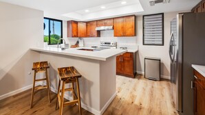 A modern kitchen with wooden cabinets, a stainless steel refrigerator, and a large island with stools. - Big Island Waikoloa Fairways B-214 2 Bedroom Condo (Waikoloa)
