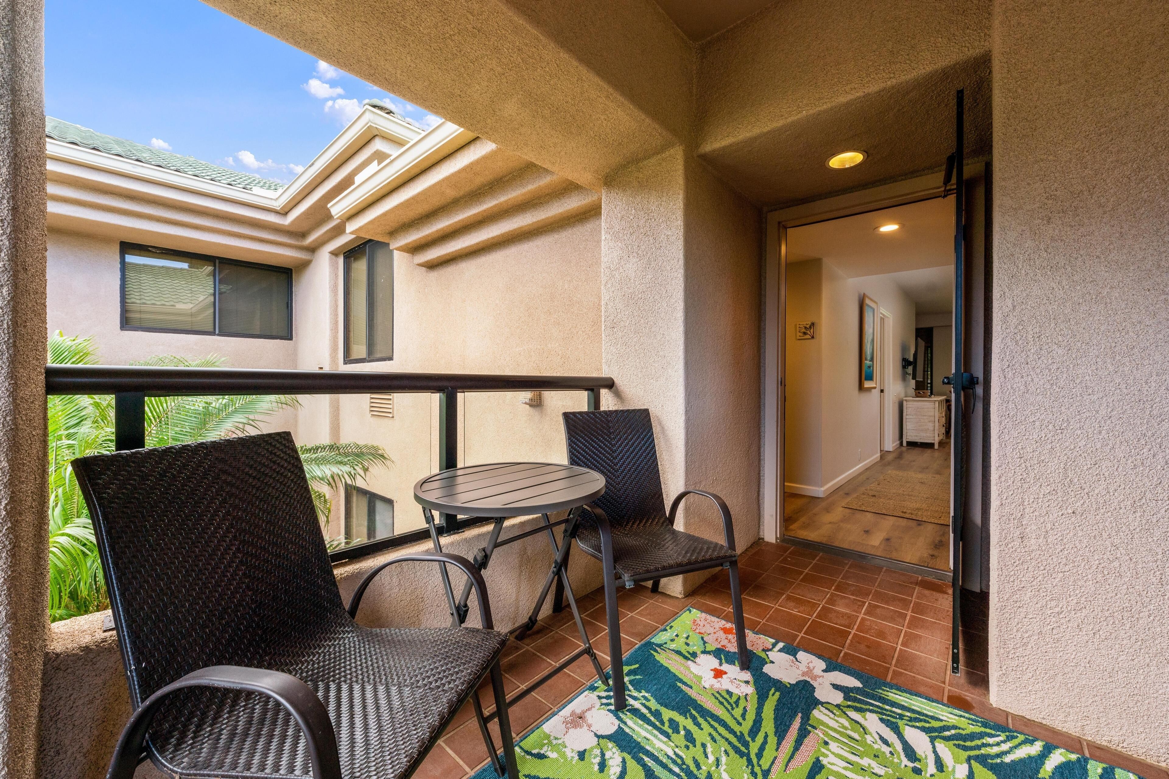 A balcony with wicker chairs, a small table, and a floral rug.