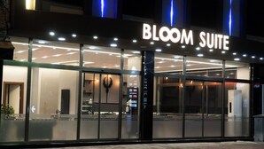 L'esterno dell'hotel Bloom Suite, con insegne illuminate, ampie vetrate e un design architettonico moderno.