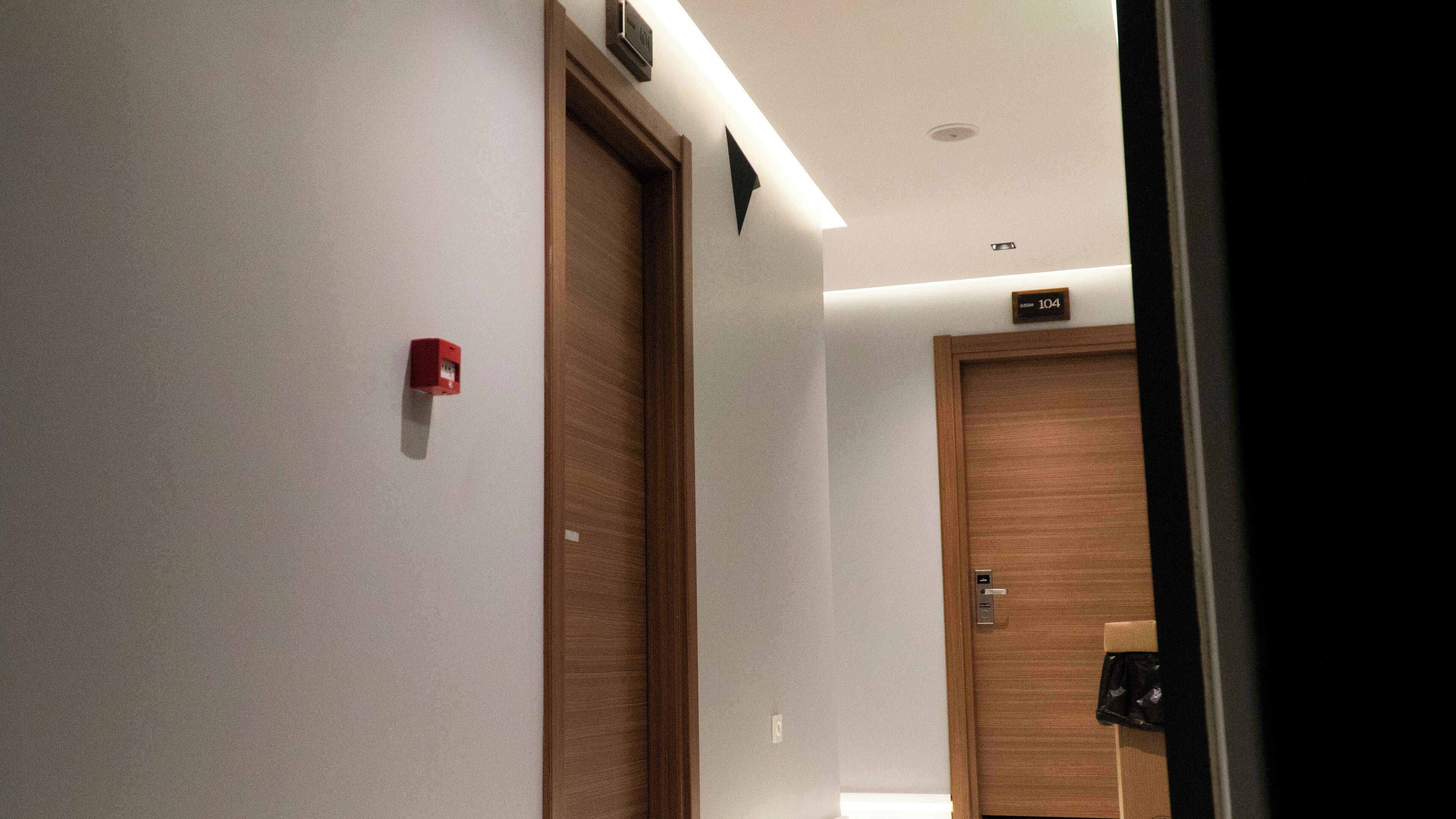A hallway with wooden doors, a red fire alarm, and a sign indicating room number 104.