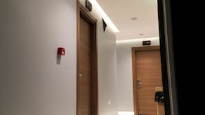 A hallway with wooden doors, a red fire alarm, and a sign indicating room number 104. - Bloom Suite (Kesan)