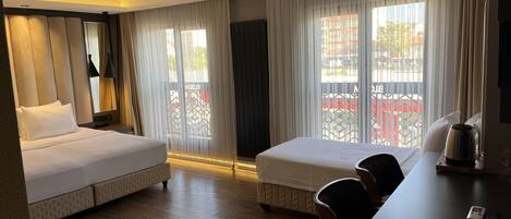 A hotel room with two beds, a desk with a kettle, and a view of the outside.