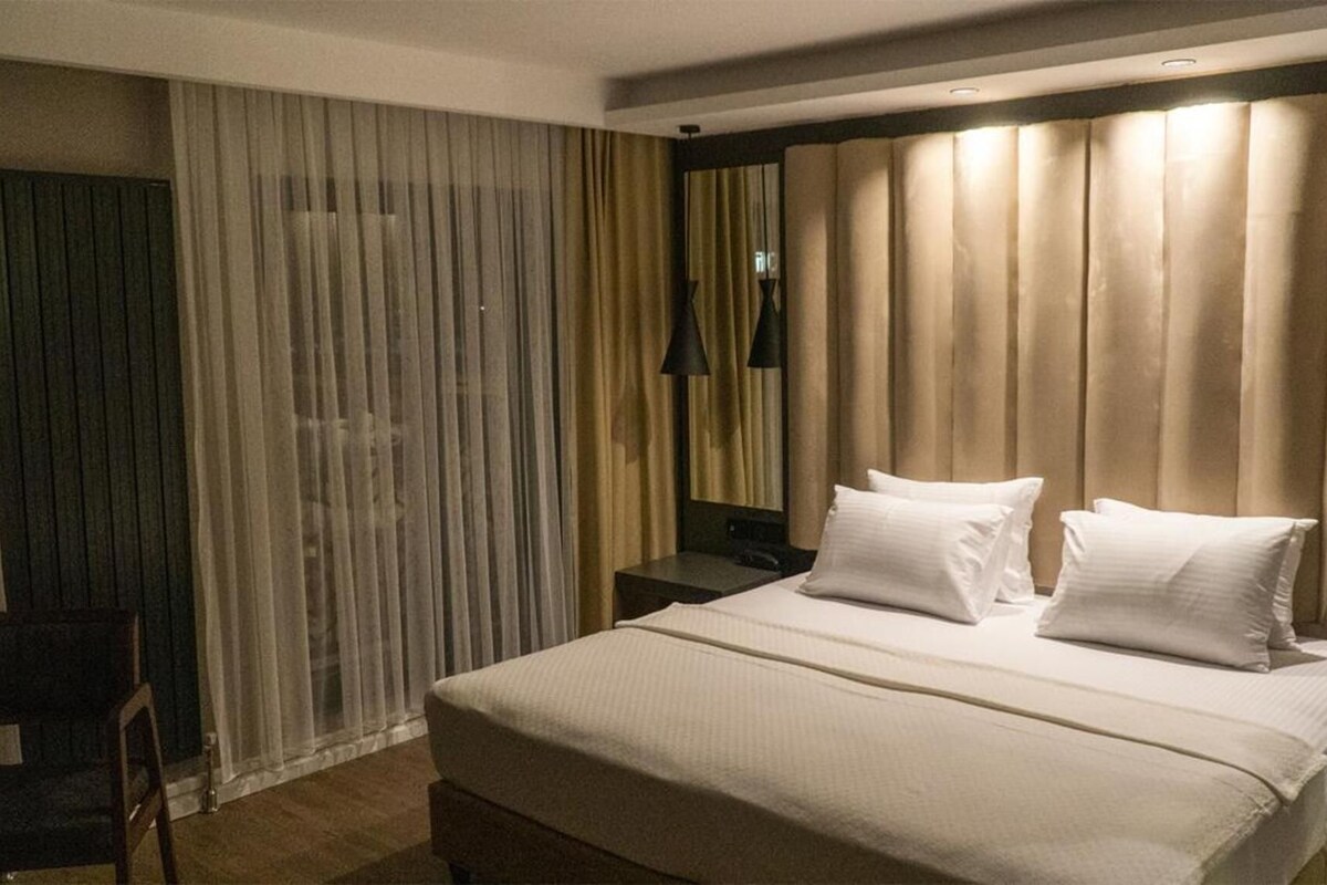 Una habitación de hotel con una cama grande, una mesita de noche, una silla y una ventana con cortinas.