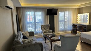 Una camera d'albergo con divano, poltrona, un tavolino, televisore e un letto.
