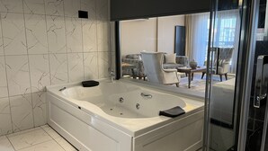 Un bagno moderno con una vasca da bagno ampia, un box doccia in vetro e vista su un'area living con divano e poltrone.