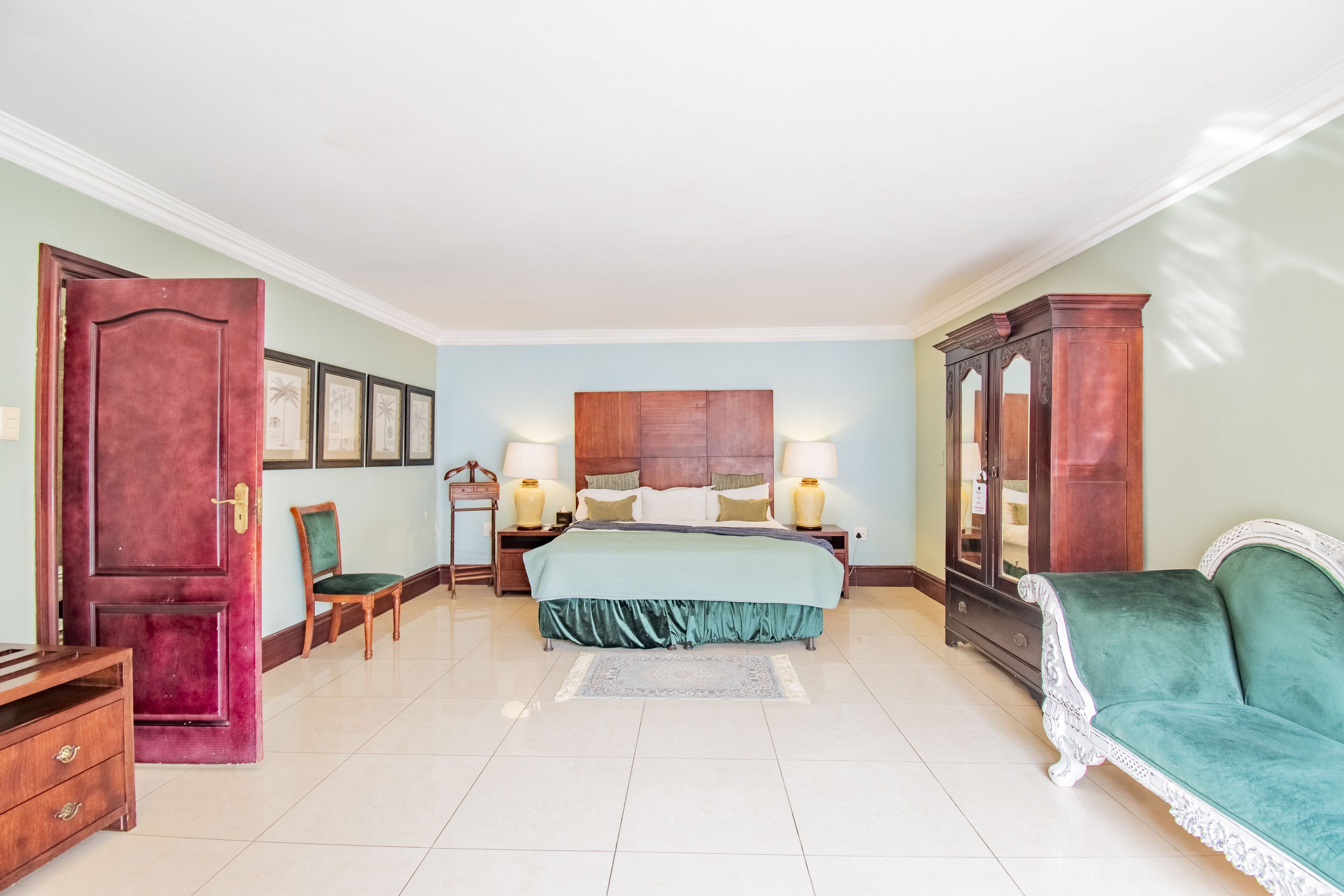Un dormitorio amplio con una cama grande, un sofá verde, un armario de madera y una mesita de noche de madera con lámparas.