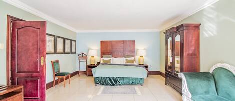 Un dormitorio amplio con una cama grande, un sofá verde, un armario de madera y una mesita de noche de madera con lámparas.