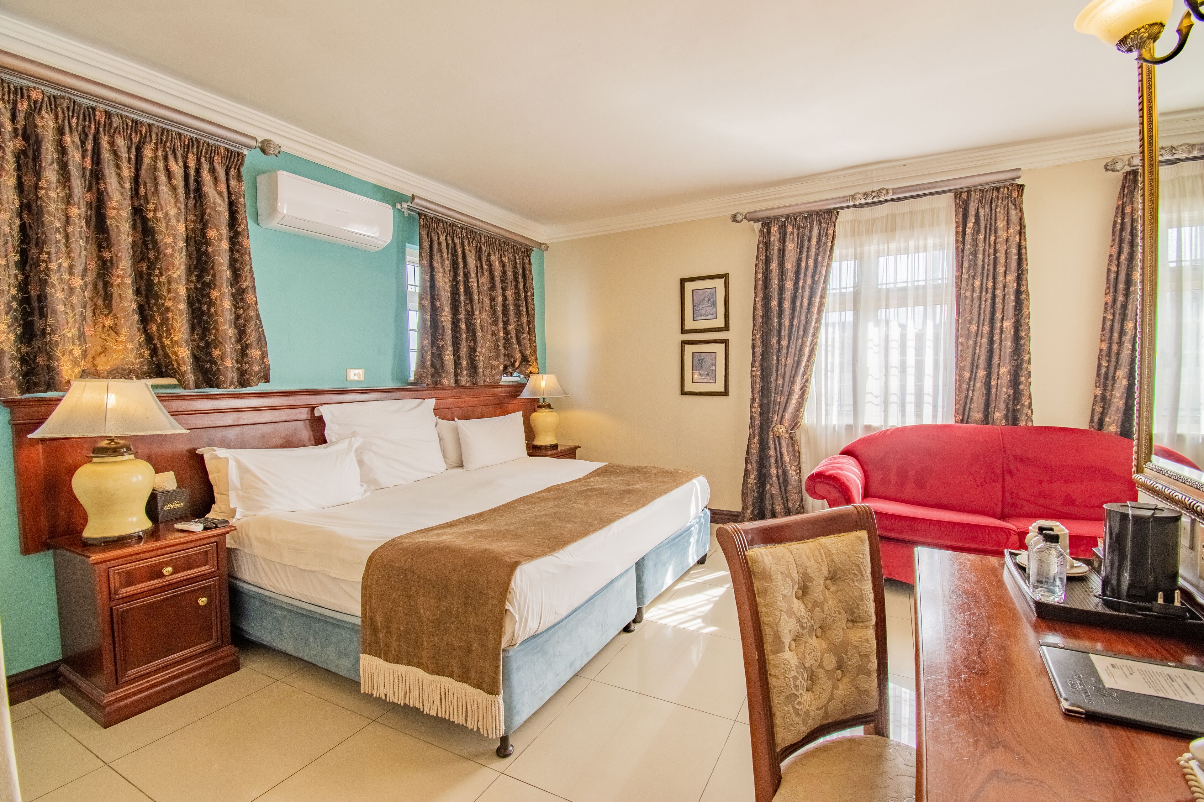 A hotel room with a large bed, a red sofa, a wooden desk, and a chandelier.