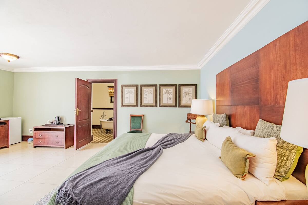Un dormitorio con cama, mesita de noche, lámpara y cuadros en la pared.